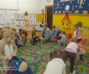 Dzieci tańczą w kole z nauczycielką w towarzystwie pluszowych zabawek.