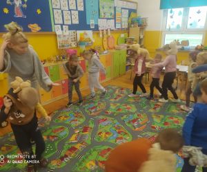 Dzieci tańczą w kole z nauczycielką w towarzystwie pluszowych zabawek.