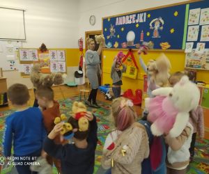 Dzieci tańczą w kole z nauczycielką w towarzystwie pluszowych zabawek.