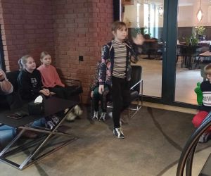 Grupa dzieci w nauczycielem siedząca i czekająca na swoją kolej do rzutu kulą