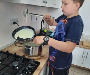 Chłopiec w granatowej koszulce rozprowadza ciasto naleśnikowe po patelni