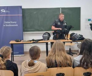 Funkcjonariusz przedstawia uczniom psa pracującego w ZK