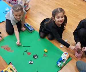 Dzieci tworzą pracę plastyczną przedstawiającą kota na dużym arkuszu zielonego papieru.