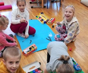 Dzieci tworzą pracę plastyczną przedstawiającą kota na dużym arkuszu zielonego papieru.