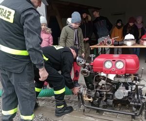 Strażak zaprezentował podłączenie węża do motopompy.