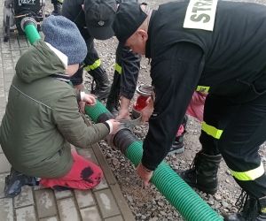 Uczeń pod opieką strażaków łączy węże gaśnicze.