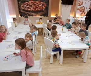 Dzieci siedzą przy stolikach i przygotowują się do zajęć plastycznych.