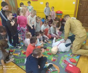 Strażak demonstruje dzieciom udzielanie pierwszej pomocy.