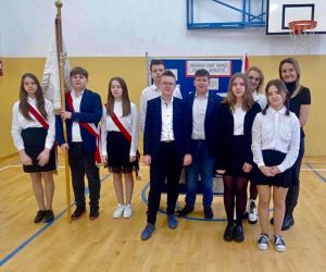 Uczniowie z wychowawcą i panią dyrektor stoją na tle dekoracji dotyczącej Żołnierzy 