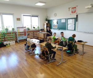 Uczennica w roli nauczyciela siedzi przed uczniami klasy I