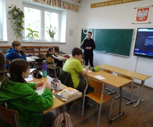 Uczeń w roli nauczyciela stoi przed siedzącymi uczniami - prowadzi lekcję