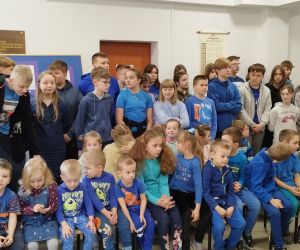 Uczniowie i nauczyciele ubrani na niebiesko podczas apelu na korytarzu szkolnym