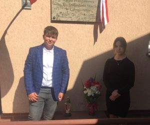 Uczennica i uczeń klasy siódmej składają kwiaty i znicz pod tablicą pamiątkową patrona szkoły