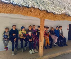 Uczniowie siedzą przed chatą wiejską