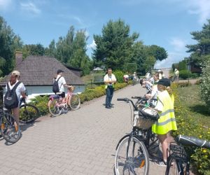 Uczniowie z rowerami stoją przed dawną kuźnią w Dziekanowie i słuchają opowieści pana Jacka Fuchsa