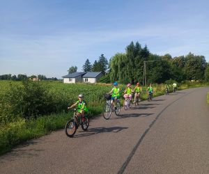 Uczniowie w kamizelkach odblaskowych jadą szosą na rowerach