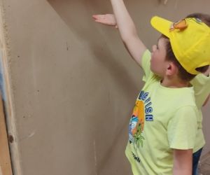 Chłopiec wyciąga rękę do papugi siedzącej wyżej