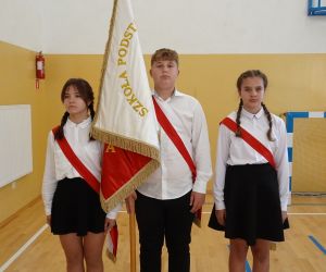 Chłopiec i dwie dziewczynki w strojach galowych ze sztandarem szkoły