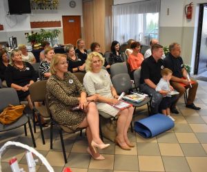 Na zdjeciu widoczna jest grupa ludzi siedzących na krzesłach, wewnątrz budynku.