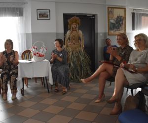 Na zdjęciu widoczna jest grupa osób siedząca na krzesłach wewnątrz budynku. 