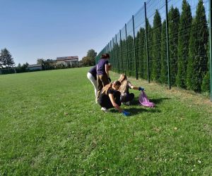 Grupa uczennic zbiera śmieci do worków na boisku