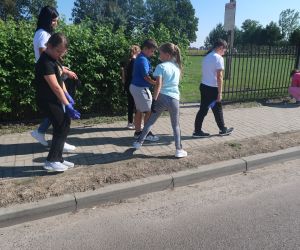 Uczniowie czwartej klasy pod opieką wychowawczyni sprzątają poboczne.