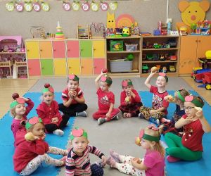 Przedszkolaki w czerwonych ubraniach oglądają trzymane w dłoniach jabłka