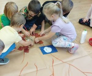 Przedszkolaki wyklejają wspólnie jesienne drzewo z bibuły i liści