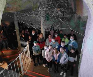 Grupa uczniów przy schodach w korytarzu kredowym. Nad nimi duża sztuczna pajęczyna z pająkiem na środku