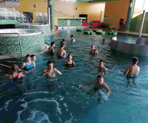 Uczniowie w strojach kąpielowych pływają w basenie