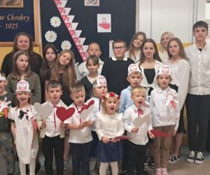 Nauczyciele i uczniowie na tle gazetki okolicznościowej