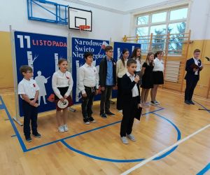 Uczeń śpiewa do mikrofonu stojąc przed szeregiem pozostałych uczniów