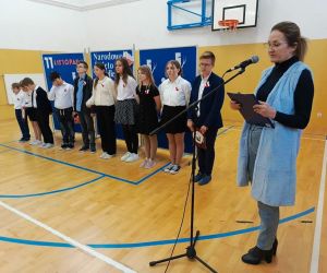 Pani dyrektor przemawia przy mikrofonie, w tle stoją uczniowie biorący udział w występie