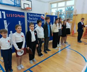 Uczniowie w strojach galowych na tle tablicy dekoracyjnej