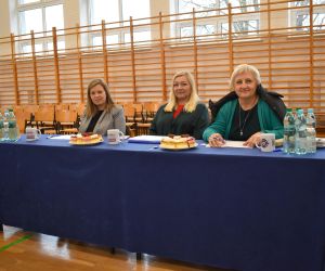 Komisja Konkursowa, trzy kobiety siedzą przy stoliku, wewnątrz budynku.