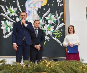 Trzy osoby stoją na scenie wewnątrz budynku.