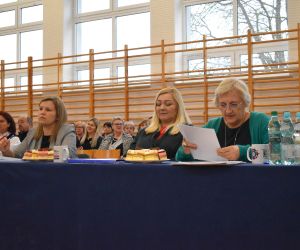 Komisja Konkursowa, trzy kobiety siedzą przy stoliku, wewnątrz budynku.