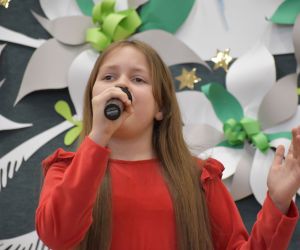 Dziewczynka na scenie wewnątrz budynku, śpiewa do mikrofonu.